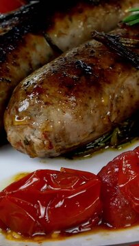 Fatty white bavarian sausages with tomato and sprig of rosemary in ceramic dish on dining table. English or German, European or American breakfast. Vertical video.
