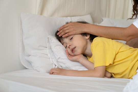 Caring Mother Checking Kid Body Temperature Touch Forehead Of Small Peaceful Sleeping Boy In Bed After Serious Disease Illness And Fever. Loving Parent Hand In Son Head. Child Healthcare And Treatment