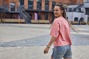 a playful girl in a pink T-shirt and short shorts poses for the camera standing on the street of the city. High quality photo