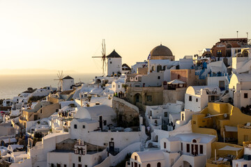 Fototapeta na wymiar Whitewashed houses and windmills in Oia in warm rays of sunset on Santorini island. Greece