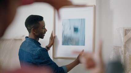 young mixed race couple moving into new house hanging picture on wall decorating home together enjoying teamwork in new apartment 4k footage