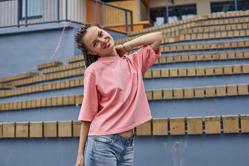 a young positive woman smiles beautifully right on camera standing outside near a stone gray staircase. High quality photo