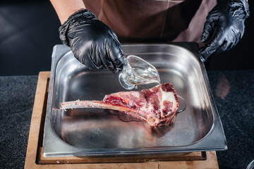 A professional chef marinates and prepares a juicy steak from a fresh piece of meat. Cooking in an mca in a gourmet restaurant.