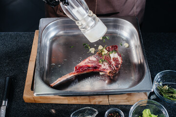 A professional chef salts a juicy steak from a fresh piece of meat. Cooking in an mca in a gourmet restaurant.