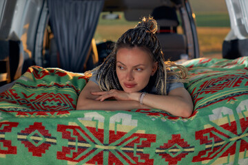 Fototapeta premium a young hippie girl lies in her car on a bright green blanket and looks away. High quality photo
