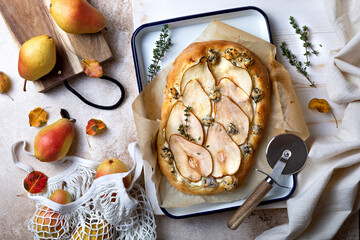 Oval pizza with pear, thyme, ricotta and blue cheese on baking paper over white wooden table