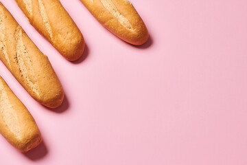 Four baked artisan whole baguettes with golden crusty floury texture on pink background with copy space. Horizontal photo.