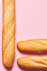 Four baked artisan whole baguettes with golden crusty floury texture on pink background with copy space. Vertical photo.