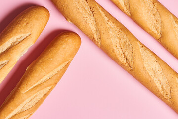 Four baked artisan whole baguettes with golden crusty floury texture on pink background with copy space. Horizontal photo.