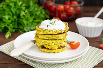 Vegetable zucchini pancakes with cheese, dill and parsley on a plate with sour cream on a dark wooden background. copy space