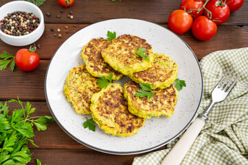 Vegetable zucchini pancakes with cheese, dill and parsley on a plate with sour cream on a dark wooden background. copy space