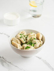 Boiled dumplings sprinkled with fresh herbs. Plate with dumplings on a light table
