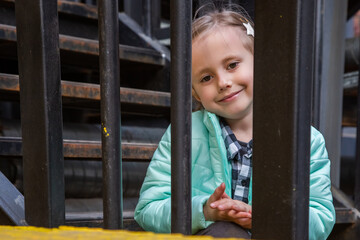 Adorable girl sits on the iron staircase with interest watching the passers-by