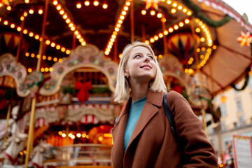 Fototapeta na wymiar blonde woman near carousel at the Christmas market