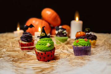 Halloween cupcakes on black background, lit candles and pumpkins in the back 