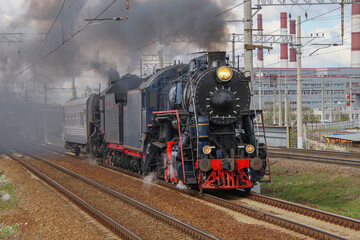 Fototapeta na wymiar A black steam locomotive with a passenger carriage rides on the railway, releasing puffs of smoke