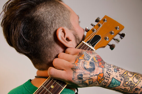 Closeup shot of tattooed man holding guitar next his face 