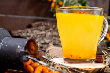 Vitamin berry tea from sea buckthorn in a glass glass, next to sea buckthorn berries. Wooden background.