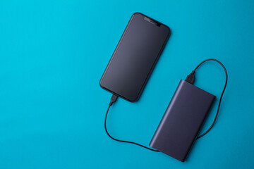 Charging a black smartphone with a frosted protective glass with purple Power Bank on turquoise background. Charge your smartphone via the USB port. Top view.