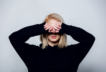 blonde in black hoodie hides a face on a white background