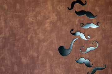 Black mustache and hat on brown leather background texture with copy space, International Men's day...