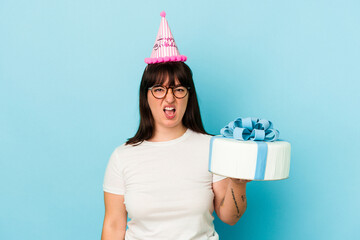 Young curvy woman celebrating her birthday isolated on blue background screaming very angry and aggressive.