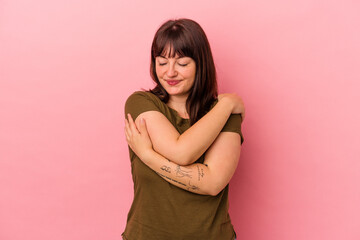 Young curvy caucasian woman isolated on pink background hugs, smiling carefree and happy.