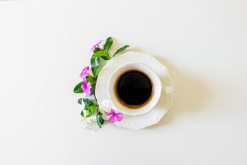 Black coffee cup, white flowers and blackberry tree leaves on white background. Flat lay, Top view. Spring concept.
