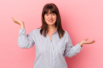 Young curvy caucasian woman isolated on pink background confused and doubtful shrugging shoulders to hold a copy space.