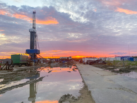 An oil field with an oil rig and wagons. Reflection in a puddle at sunset. Oil industry.