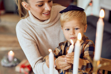 Small Jewish boy and mother light menorah candles while celebrating Hanukkah at home.