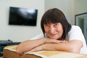 Portrait of a beautiful elderly woman smiling while sitting on the sofa at home enjoying retirement in casual clothes during the day. Caucasian grandmother resting