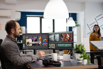 Video editor man editing movie project working in start up creativity multimedia agency office sitting at pc with two monitors. Editor processing film montage using post production software
