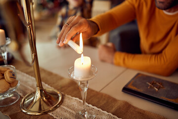 Fototapeta na wymiar Close-up of man lighting up candle while celebrating Hanukkah at home.