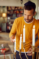 Jewish man lights traditional Hanukkah candles at home.