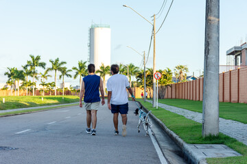 Homens caminham com cão Dalmata ao entardecer