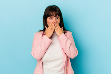 Young curvy caucasian woman isolated on blue background shocked covering mouth with hands.