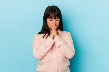 Young curvy caucasian woman isolated on blue background praying, showing devotion, religious person...