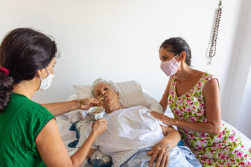 Mulher idosa doente de cama ap&oacute;s queda com bra&ccedil;o quebrado recebe cuidados de filha e amiga
