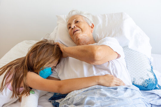 Mulher idosa doente de cama ap&oacute;s queda com bra&ccedil;o quebrado recebe carinho de neta no leito 