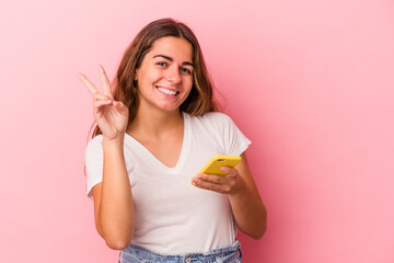 Young caucasian woman using mobile phone isolated on pink background  showing number two with fingers.