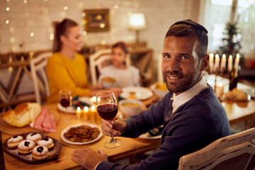 Happy Jewish man drinks wine while having meal with his family on Hanukkah.