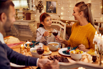 Happy Jewish mother and daughter toast during Hanukkah meal at dining table.