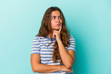 Young caucasian woman isolated on blue background  looking sideways with doubtful and skeptical expression.