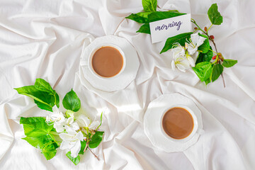Black coffee cup, white flowers and blackberry tree leaves on white background. Flat lay, Top view. Spring concept.