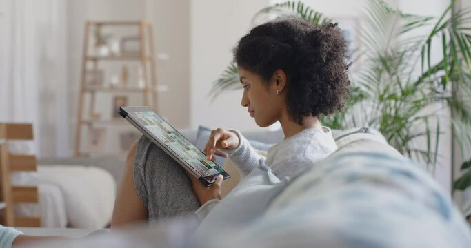 young woman browsing online using tablet computer scrolling looking at social media pictures with mobile touchscreen technology relaxing on sofa at home 4k