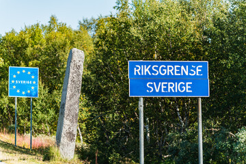 Fototapeta premium State border between Norway and Sweden in Northern Sweden, mountains in Lappland. Mile stone with Swedish text and blur road sign with Norwegian words, European Union road sign on Swedish