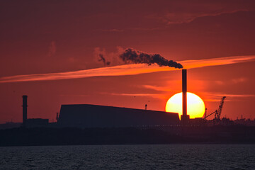 Beautiful telephoto view of epic orange sunset over Dublin port and Sun aligned with Covanta Plant (Dublin Waste to Energy) seen from west pier of Dun Laoghaire harbor, Dublin, Ireland. Soft focus