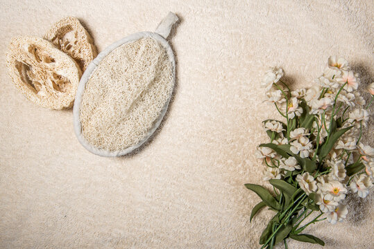 Esponja de lufa y dos discos cortados de lufa sobre un fondo beige con flores. Cambios para un ba&ntilde;o cero residuos sin pl&aacute;stico.