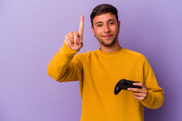 Young caucasian man holding game controller isolated on purple background  showing number one with finger.